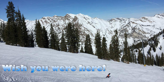 Person snowboarding down a mountain slope with "Wish you were here!" text