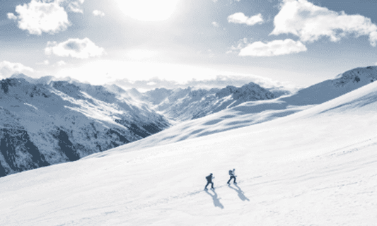 Two people hiking in snow up a mountain side