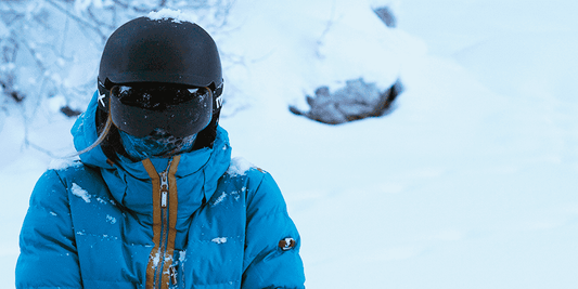 Woman wearing black snow goggles and black snow helmet, with a blue snow jacket 